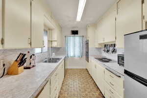 Kitchen with stainless steel appliances, light countertops, cream cabinetry, light flooring, and backsplash