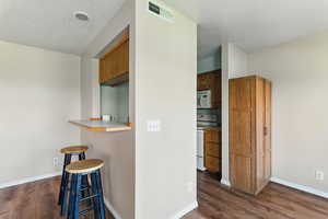 Kitchen featuring white appliances, a breakfast bar, dark wood finished floors, light countertops, and a textured ceiling