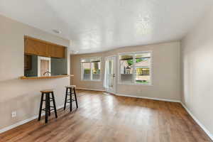 Kitchen featuring a breakfast bar area, brown cabinetry, wood finished floors, a peninsula, and a textured ceiling