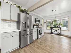 Kitchen with stainless steel appliances, light countertops, tasteful backsplash, light wood finished floors, and beam ceiling