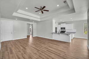 Unfurnished living room featuring a raised ceiling, a ceiling fan, light wood-style flooring, and recessed lighting