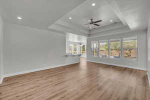 Unfurnished living room featuring a raised ceiling, light wood-style floors, ceiling fan, recessed lighting, and a chandelier