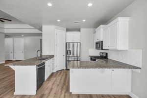 Kitchen featuring appliances with stainless steel finishes, a peninsula, stone countertops, light wood-style flooring, and recessed lighting