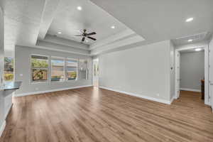 Unfurnished living room with a textured ceiling, light wood-type flooring, ceiling fan, a tray ceiling, and recessed lighting