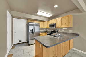 Kitchen featuring appliances with stainless steel finishes, a peninsula, dark countertops, and light brown cabinetry