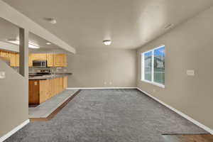 Kitchen with light brown cabinets, light carpet, appliances with stainless steel finishes, a peninsula, and light tile patterned floors
