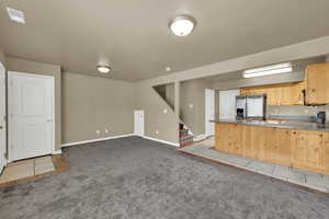 Kitchen featuring stainless steel fridge with ice dispenser, carpet, a peninsula, light brown cabinetry, and tile patterned floors