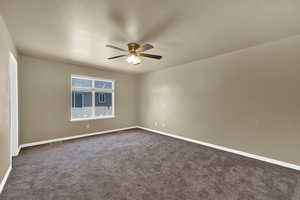 Empty room featuring ceiling fan and dark carpet