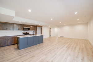 Kitchen featuring stainless steel appliances, recessed lighting, light wood finished floors, light countertops, and a center island with sink