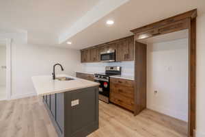 Kitchen with stainless steel appliances, an island with sink, light wood-style flooring, recessed lighting, and light countertops