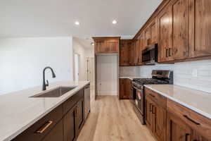 Kitchen with stainless steel appliances, light wood-style floors, tasteful backsplash, recessed lighting, and brown cabinets