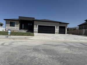 View of front facade featuring stone siding, a garage, stucco siding, and driveway