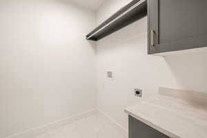 Laundry area with hookup for an electric dryer, washer hookup, cabinet space, and light tile patterned floors
