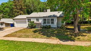 Single story home featuring a garage, a chimney, a front lawn, and concrete driveway