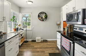 Kitchen with stainless steel appliances, dark wood-style flooring, tasteful backsplash, and white cabinets