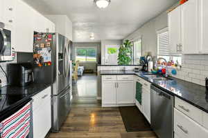Kitchen with appliances with stainless steel finishes, dark wood-type flooring, tasteful backsplash, white cabinetry, and a peninsula