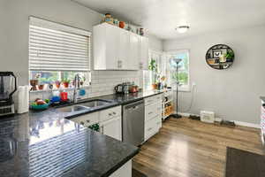 Kitchen with stainless steel dishwasher, white cabinets, backsplash, and dark wood-type flooring
