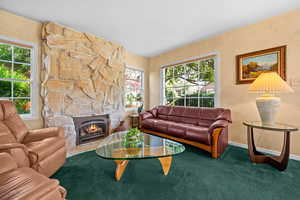 Living room featuring hardwood floors under the carpet, a Honey Onyx stone fireplace with gas fireplace insert with remote control, lots of natural east and northern natural light