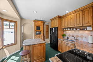 Kitchen with black appliances, built in microwave and TV, a kitchen island with bar stool seating, open shelves,  tile backsplash and canned lights with dimmers