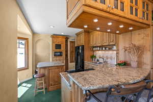 Kitchen with granite countertops, black appliances, a breakfast bar, under cabinet lighting with dimmers and an island with seating