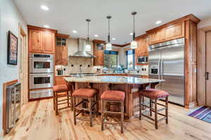Kitchen featuring built in appliances, wall chimney range hood, a warming drawer, beverage cooler, and light wood-type flooring