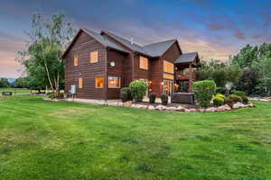 Back of property at dusk with a balcony, a yard, and a hot tub
