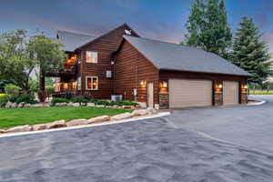 Property exterior at dusk with a balcony, asphalt driveway, a yard, stone siding, and a garage