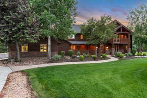 View of front of house with stone siding, a lawn, a balcony, and a shingled roof