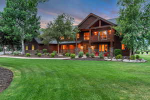Back of house featuring a balcony, stone siding, a lawn, covered porch, and roof with shingles