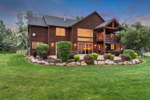 Back of property at dusk featuring a patio area, a lawn, a balcony, and roof with shingles