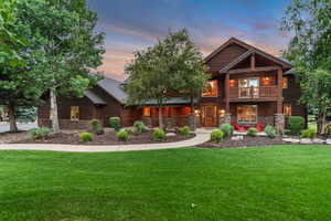 Log-style house with stone siding, a balcony, and a lawn