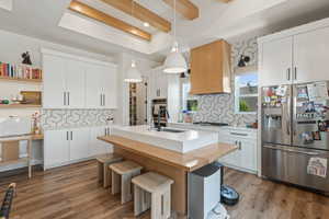 Kitchen featuring appliances with stainless steel finishes, light wood-type flooring, tasteful backsplash, light countertops, and beam ceiling