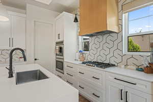 Kitchen featuring custom range hood, appliances with stainless steel finishes, decorative backsplash, and white cabinetry
