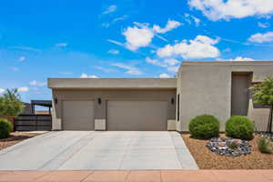 Pueblo-style house featuring an attached garage, concrete driveway, and stucco siding