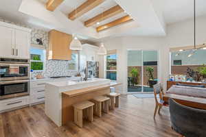 Kitchen featuring stainless steel appliances, decorative backsplash, light countertops, an island with sink, and beamed ceiling