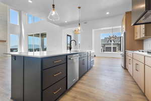 Kitchen with stainless steel appliances, exhaust hood, a center island with sink, light countertops, and recessed lighting