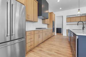 Kitchen featuring stainless steel appliances, light wood-type flooring, light countertops, backsplash, and decorative light fixtures