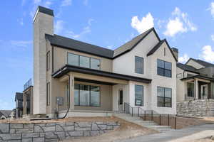 Back of house featuring a chimney, stucco siding, stone siding, and covered porch