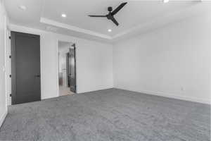 Unfurnished bedroom with a raised ceiling, recessed lighting, carpet floors, a ceiling fan, and ensuite bathroom
