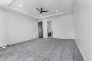 Empty room with a tray ceiling, a ceiling fan, recessed lighting, and carpet flooring
