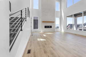 Unfurnished living room with a high ceiling, light wood-style flooring, stairs, and a fireplace