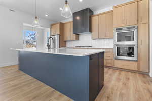 Kitchen with stainless steel appliances, a kitchen island with sink, light countertops, light brown cabinets, and backsplash
