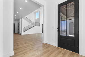 Foyer entrance with stairway, wood finished floors, and recessed lighting