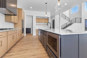 Kitchen featuring appliances with stainless steel finishes, light brown cabinetry, range hood, light wood-type flooring, and light countertops