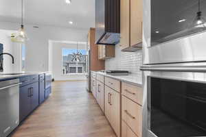 Kitchen featuring appliances with stainless steel finishes, light wood-type flooring, decorative backsplash, a chandelier, and light countertops