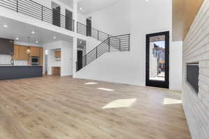 Unfurnished living room featuring a high ceiling, a fireplace, light wood-style floors, stairs, and recessed lighting