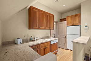 Kitchen featuring freestanding refrigerator, dishwashing machine, brown cabinetry, and light wood-style floors
