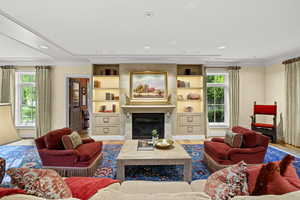 Living area with crown molding, healthy amount of natural light, wood finished floors, a glass covered fireplace, and recessed lighting