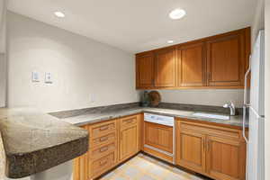 Kitchen featuring paneled dishwasher, brown cabinets, recessed lighting, freestanding refrigerator, and a peninsula