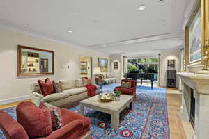 Living area featuring light wood-style flooring, crown molding, recessed lighting, and a fireplace with flush hearth